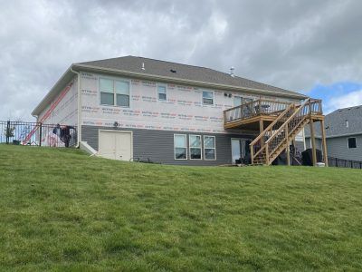 Suburban house with white siding and wooden stairs on a grassy hill under a cloudy sky