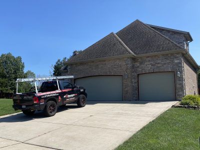 Black pickup truck parked in front of a two-car garage of a stone house on a sunny day