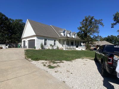 White house with gray roof, gravel driveway, and parked black truck under a clear blue sky