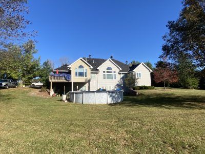 House with screened porch and above-ground pool on a grassy yard under a blue sky