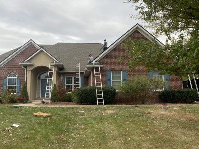 Brick suburban house with ladders leaning against the front porch and roof, suggesting exterior work