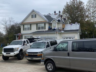 Snow-dusted house with roof work and three parked vehicles in the driveway
