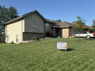 Suburban house with a for-sale sign on the lawn and a car parked in the driveway