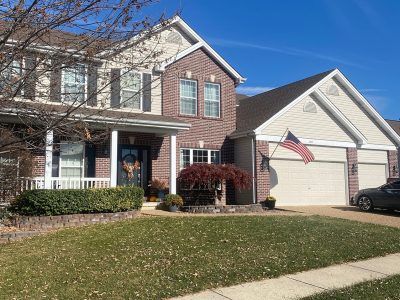 Suburban two-story brick house with a white garage and American flag, front lawn in daylight