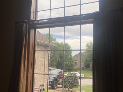 View through a window with curtains, showing a suburban driveway, parked vehicles, and a house across the street.