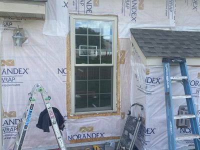 House siding under construction with a window, ladder, and tools against Tyvek house wrap