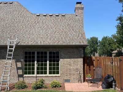 Brick house patio with a ladder, large window, chimney, and wooden fence under a blue sky