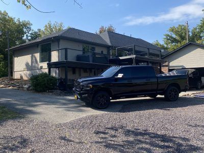 Black pickup truck parked in front of a beige two-story house with a carport and gravel driveway