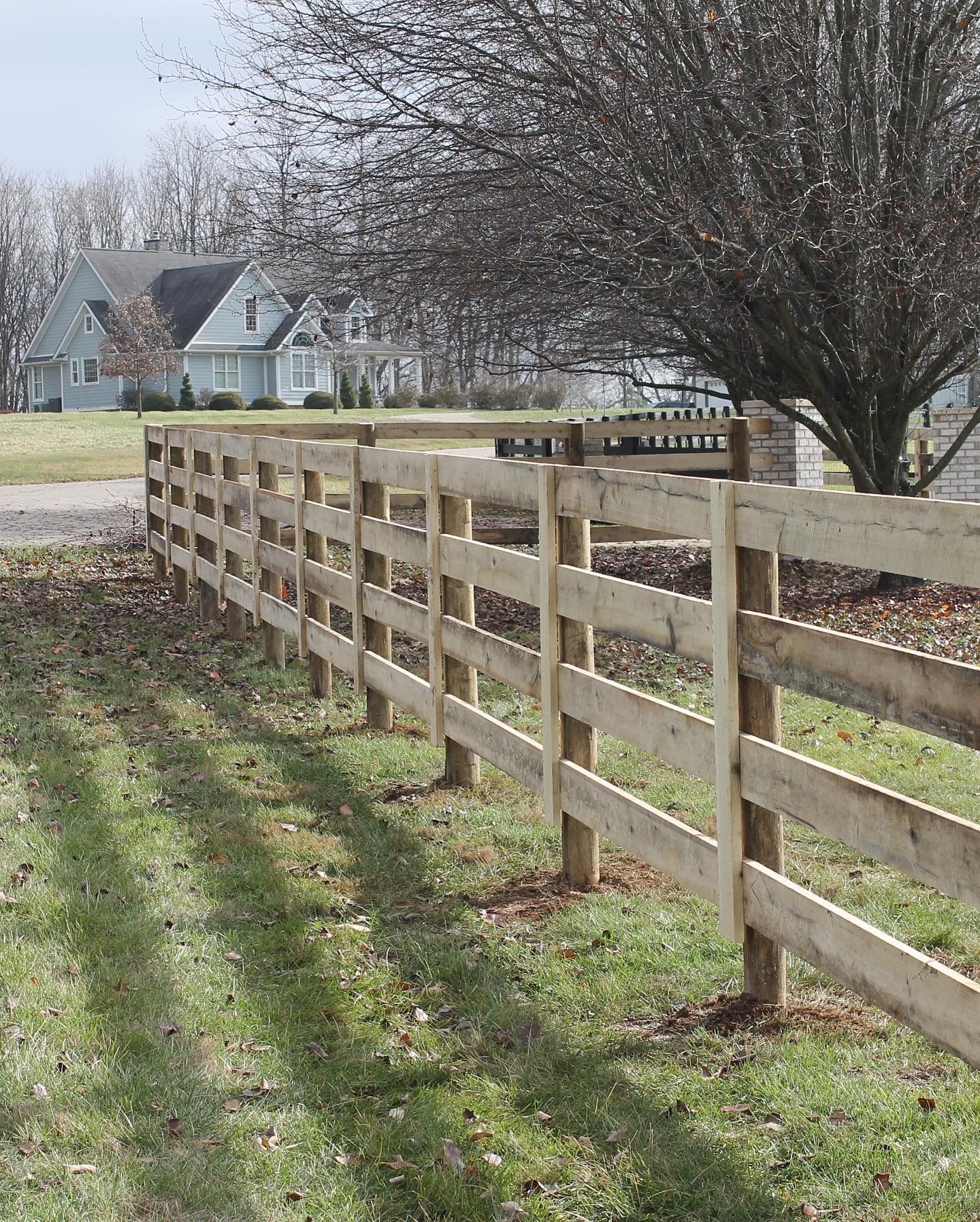 a wooden fence surrounds a grassy field in front of a house — Lexington, KY — Chafin Fence LLC