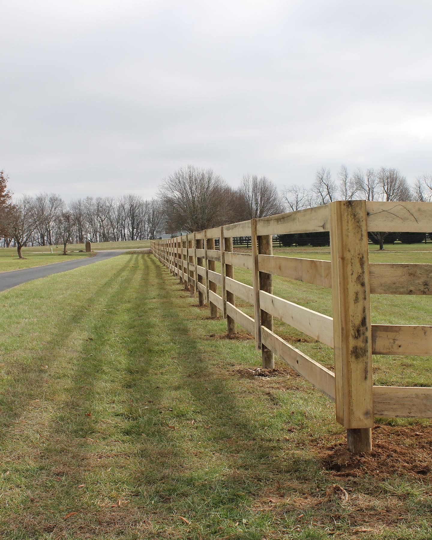 a wooden fence surrounds a grassy field next to a road — Lexington, KY — Chafin Fence LLC