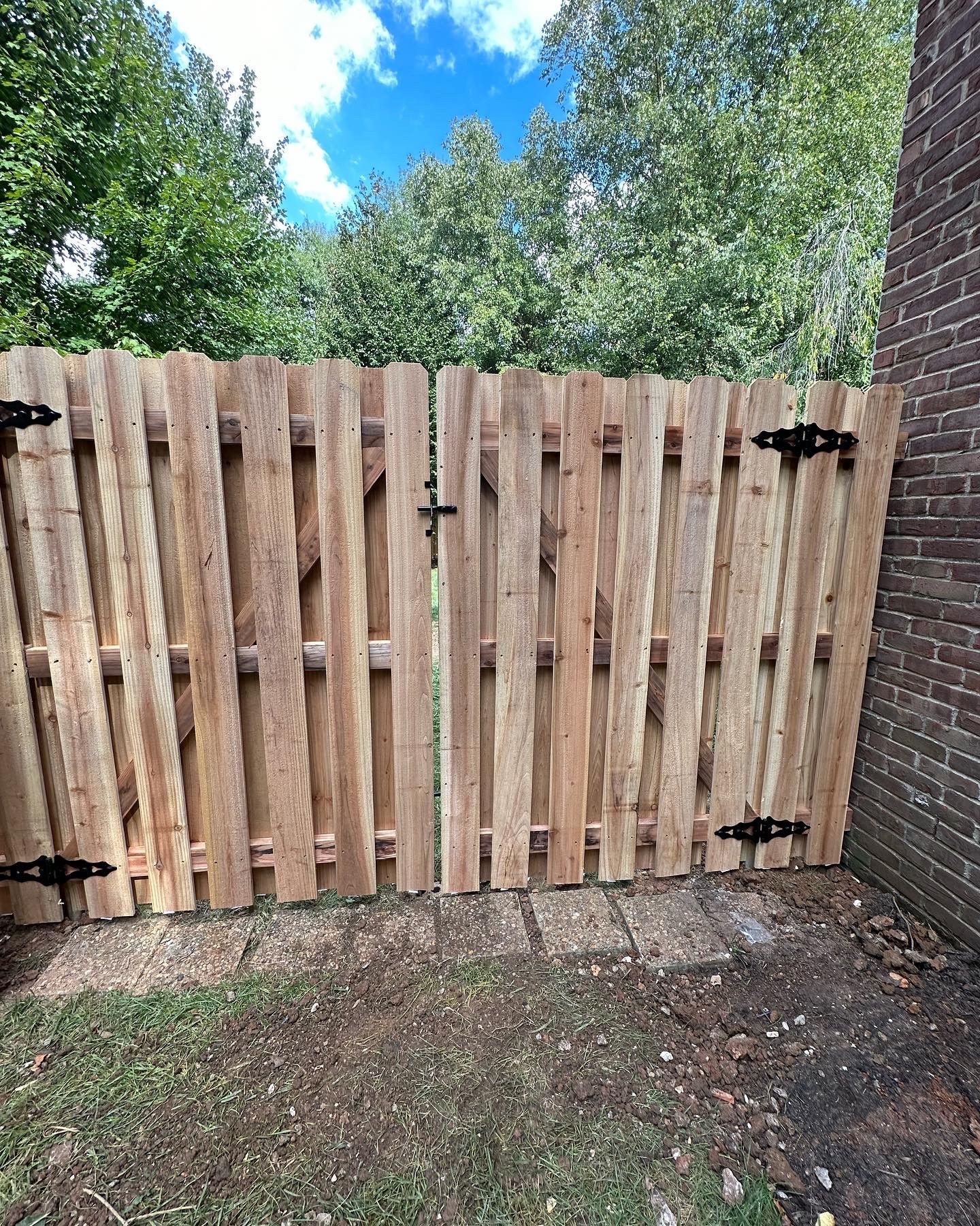 a wooden fence with a gate is sitting next to a brick building — Lexington, KY — Chafin Fence LLC