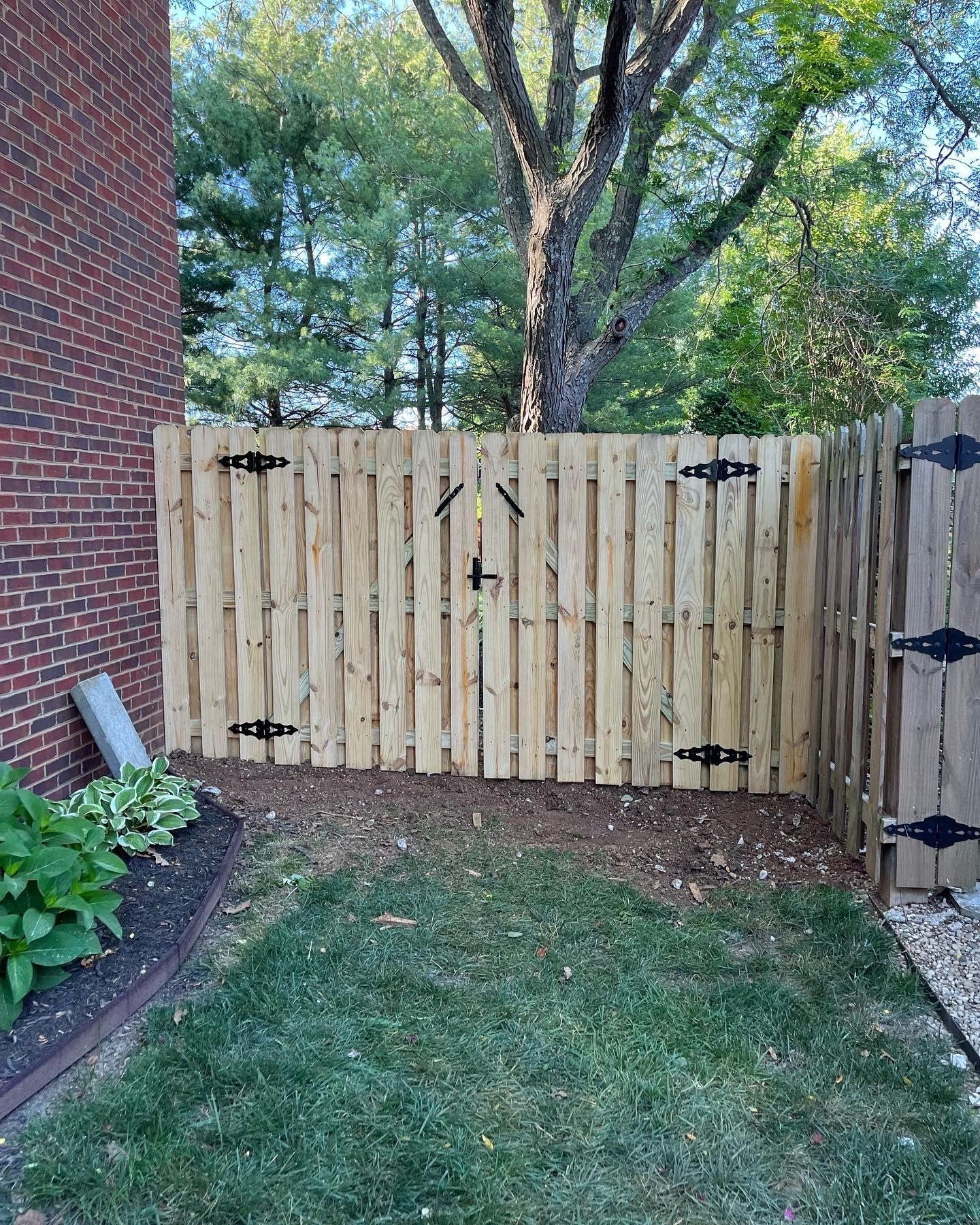 a wooden fence with a gate in the backyard next to a brick building .