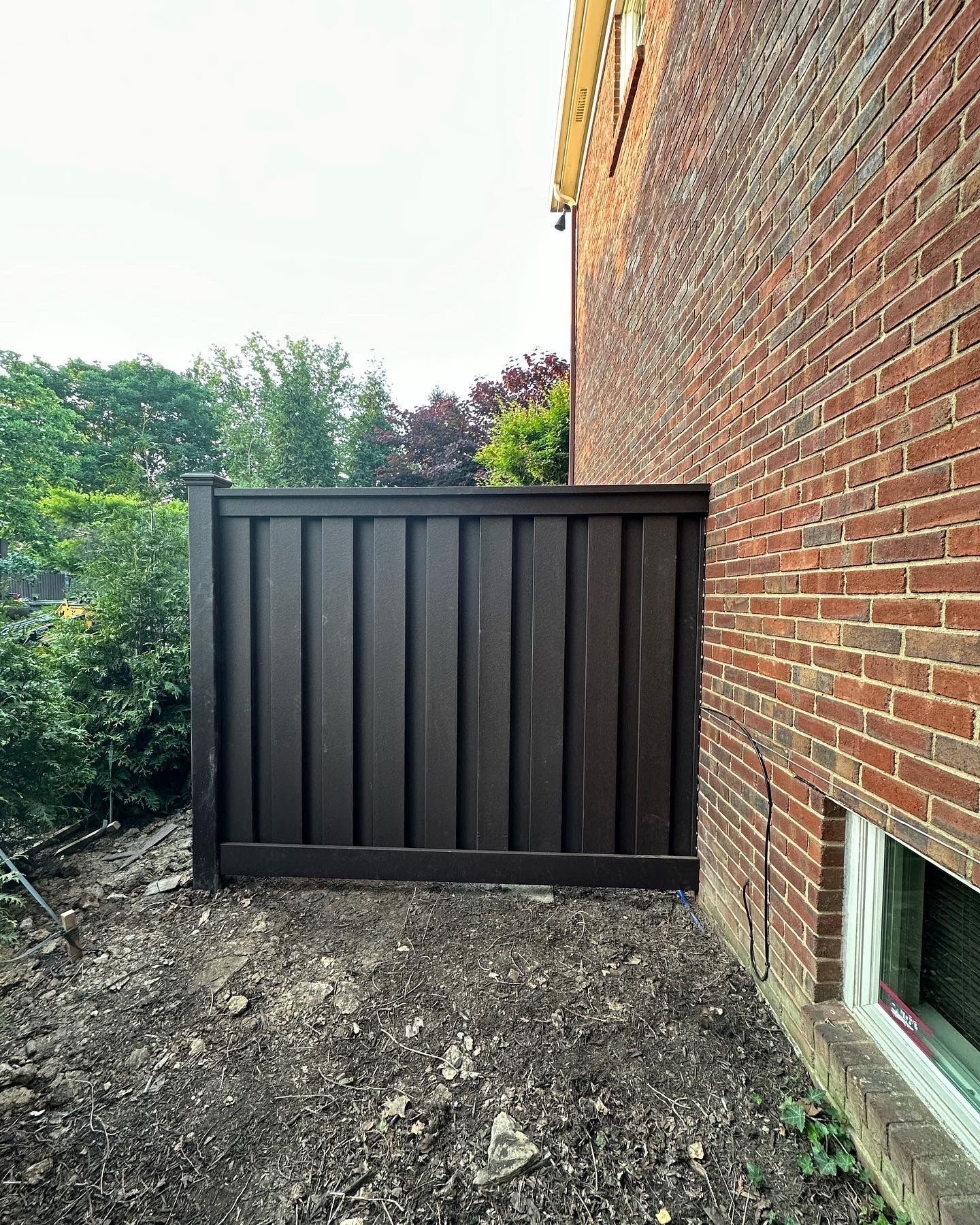 a wooden fence is sitting on the side of a brick building — Lexington, KY — Chafin Fence LLC