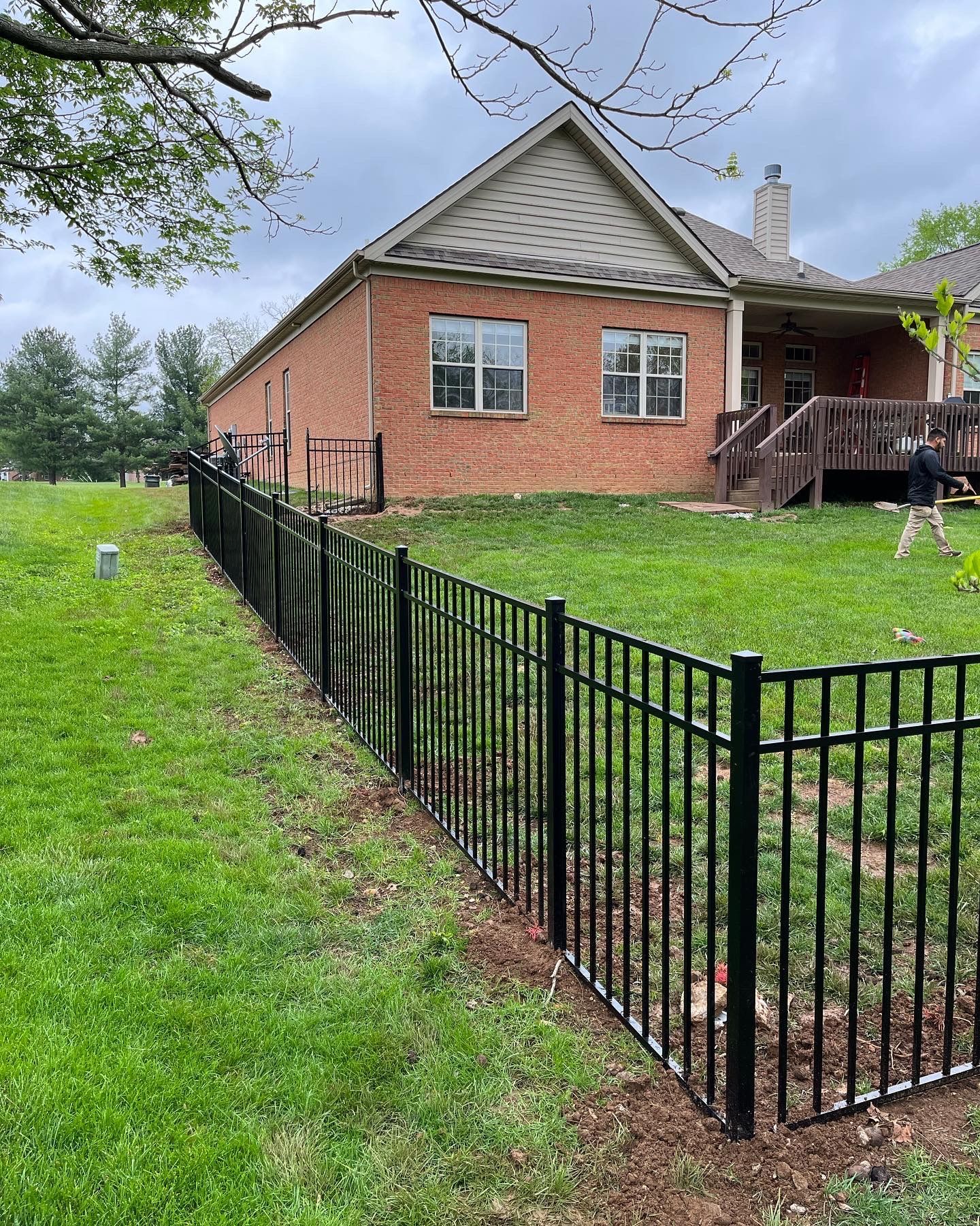 a black fence surrounds a lush green yard in front of a brick house Modern House with Fence — Lexington, KY — Chafin Fence LLC