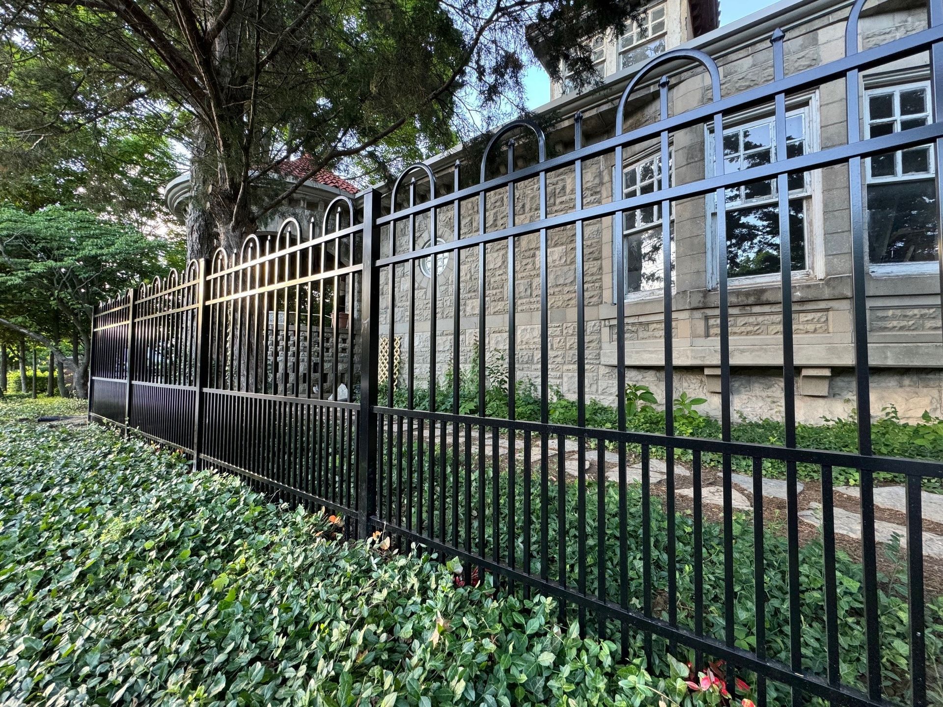 A black wrought iron fence is surrounded by bushes and trees in front of a building.