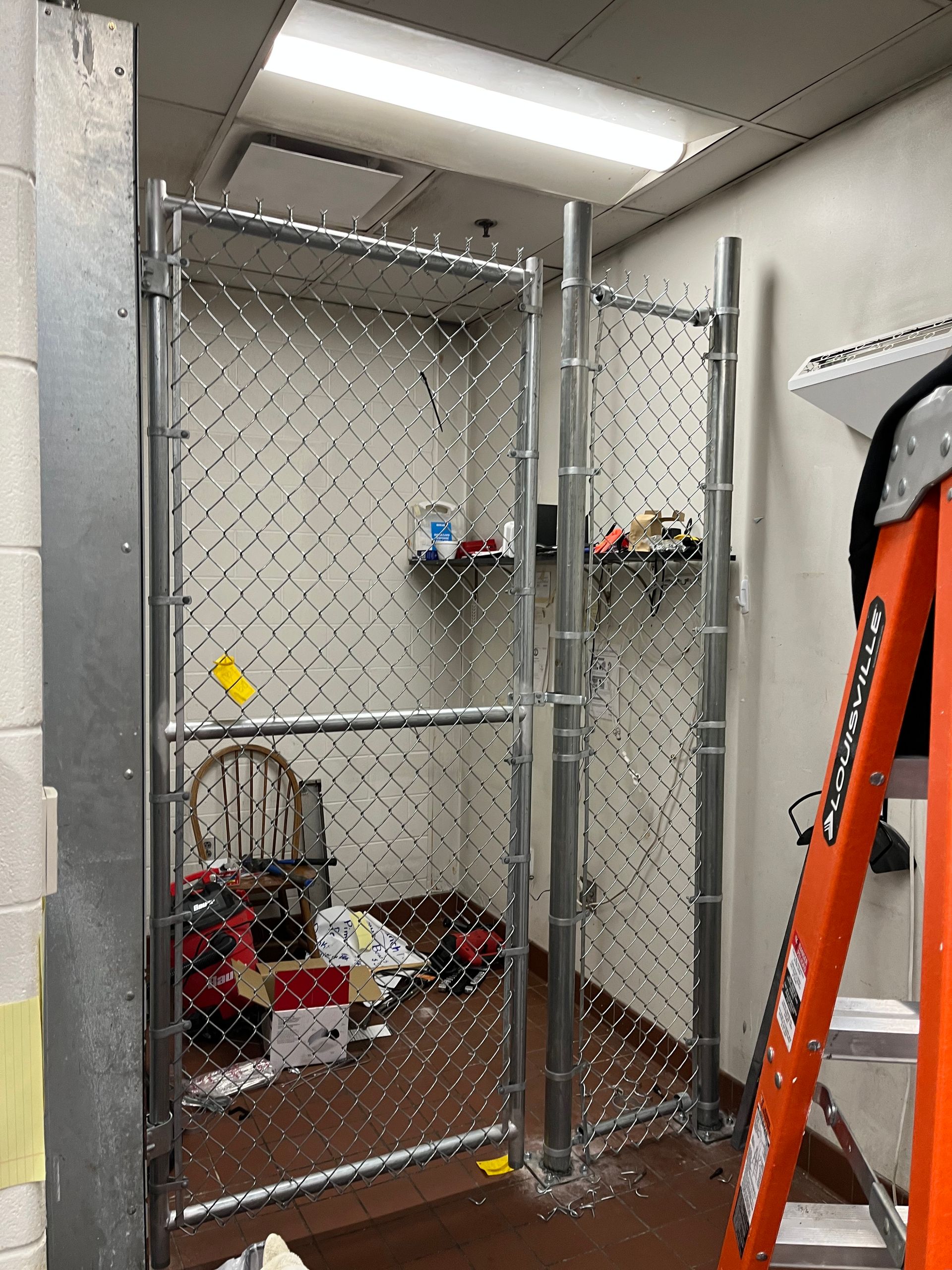 a chain link fence is being installed in a room with a ladder — Lexington, KY — Chafin Fence LLC