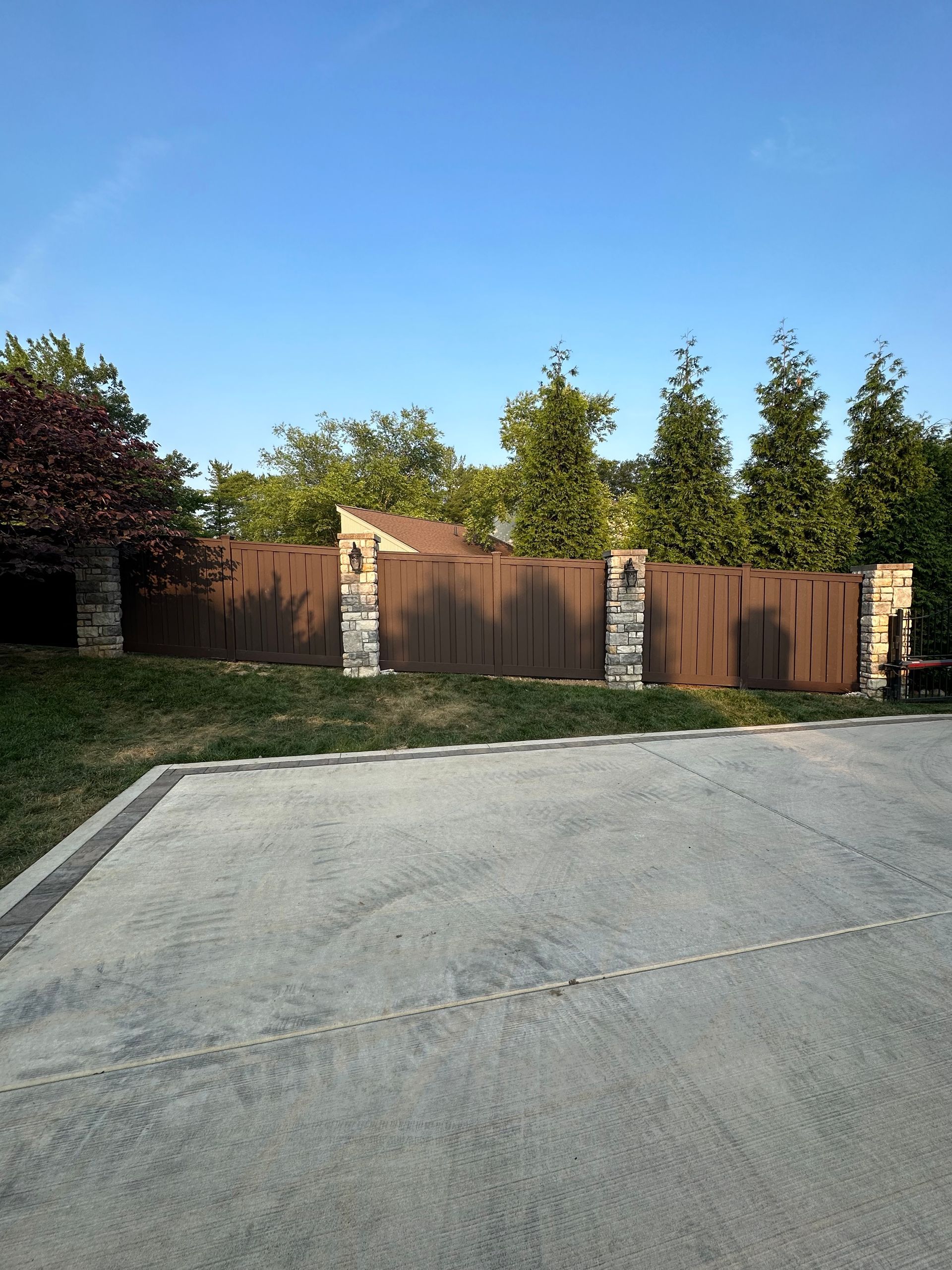 a wooden fence is surrounded by trees and a concrete driveway — Lexington, KY — Chafin Fence LLC