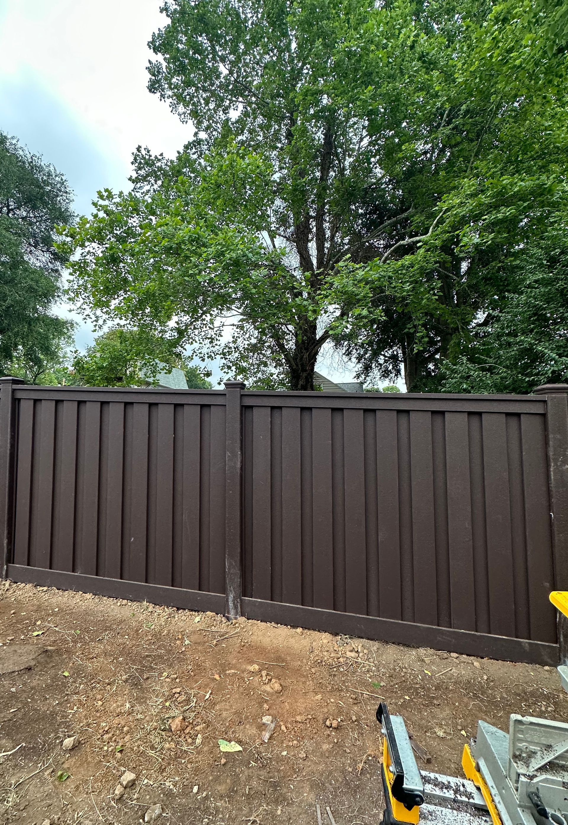 a brown fence with trees in the background and a table saw in the foreground — Lexington, KY — Chafin Fence LLC