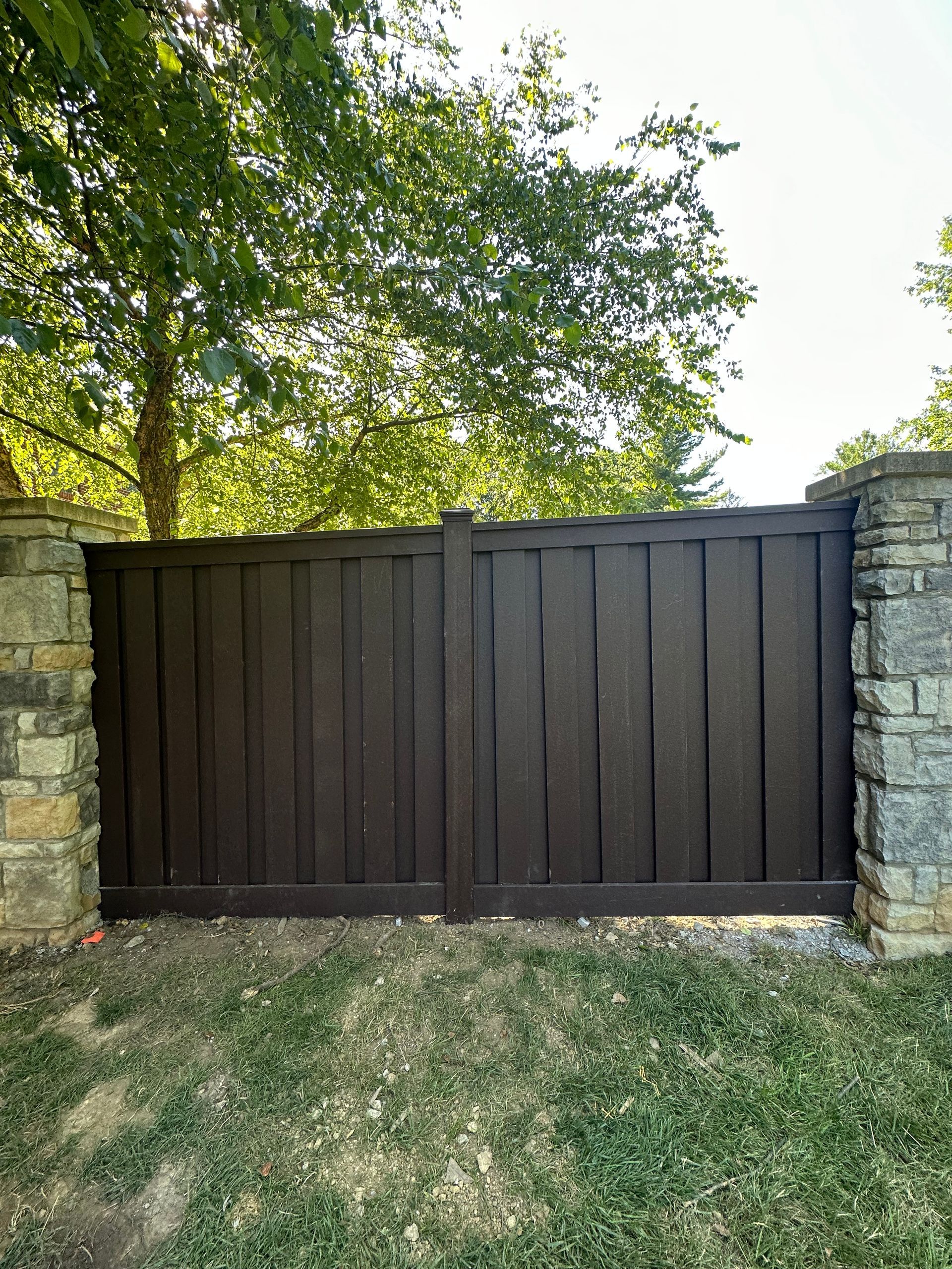 A wooden gate is sitting in the middle of a lush green field next to a stone wall – Lexington, KY - Chafin Fence LLC
