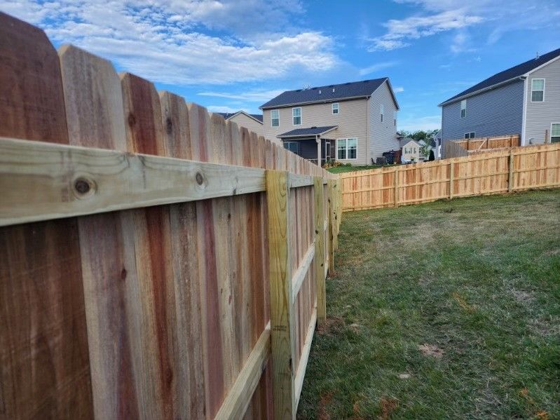 A wooden fence in a backyard with a house in the background.