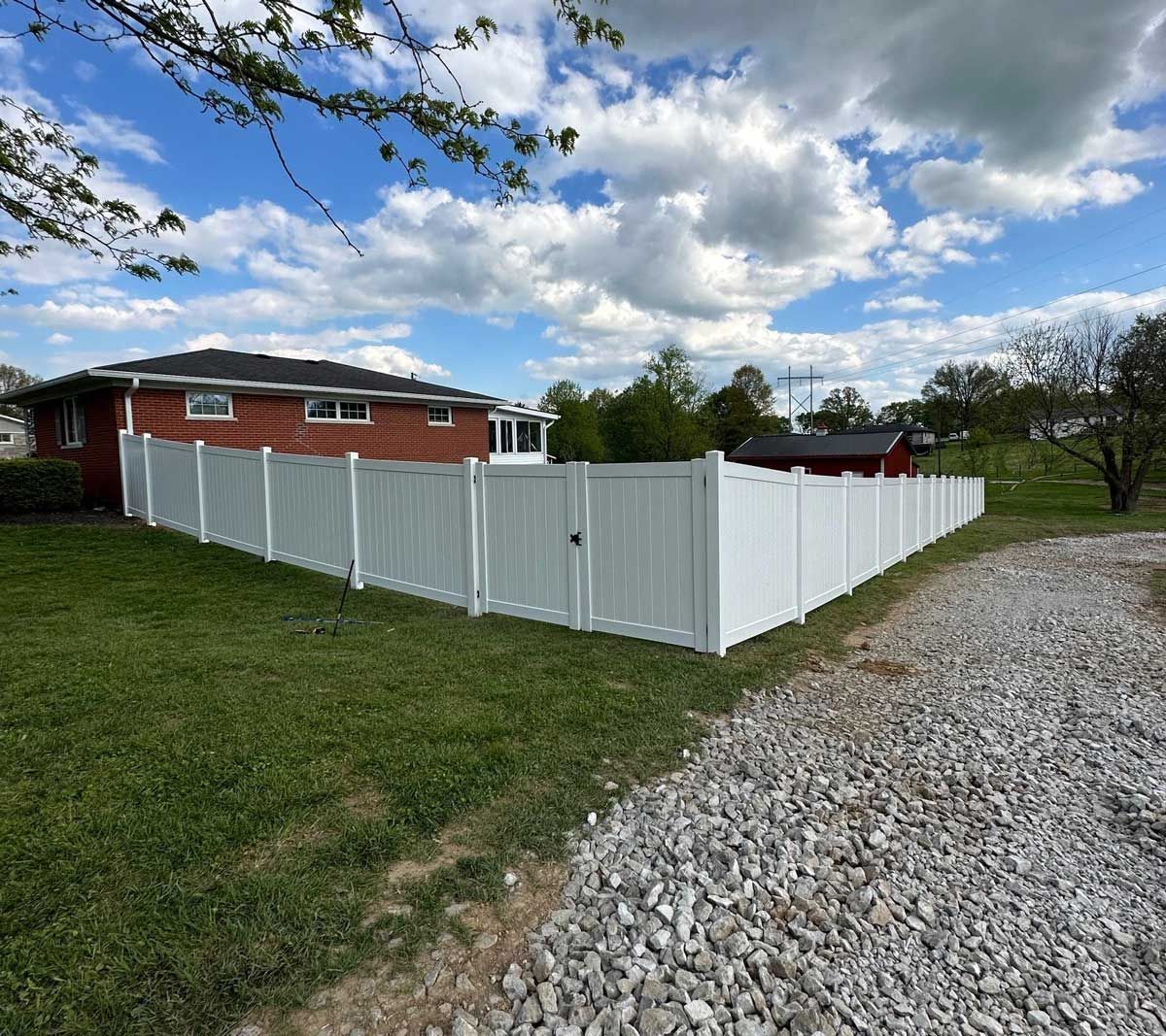 A white fence is surrounding a brick house.
