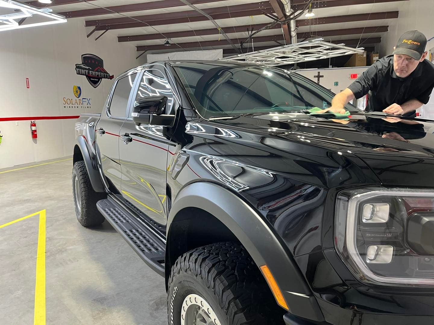 A man is cleaning the hood of a black truck in a garage.