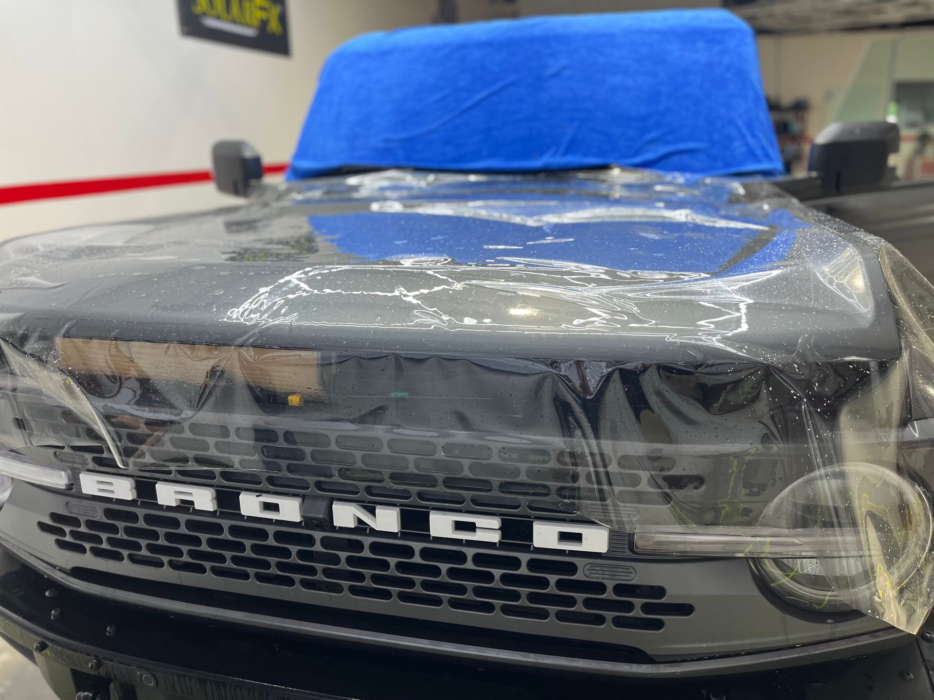 The front of a black ford bronco is covered in plastic.