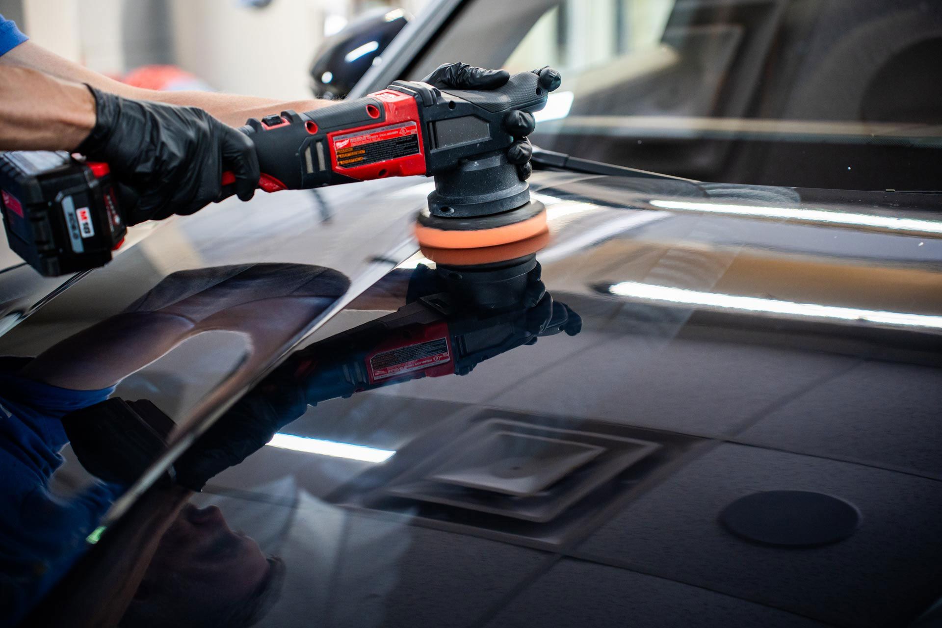 A man is polishing the hood of a car with a machine.