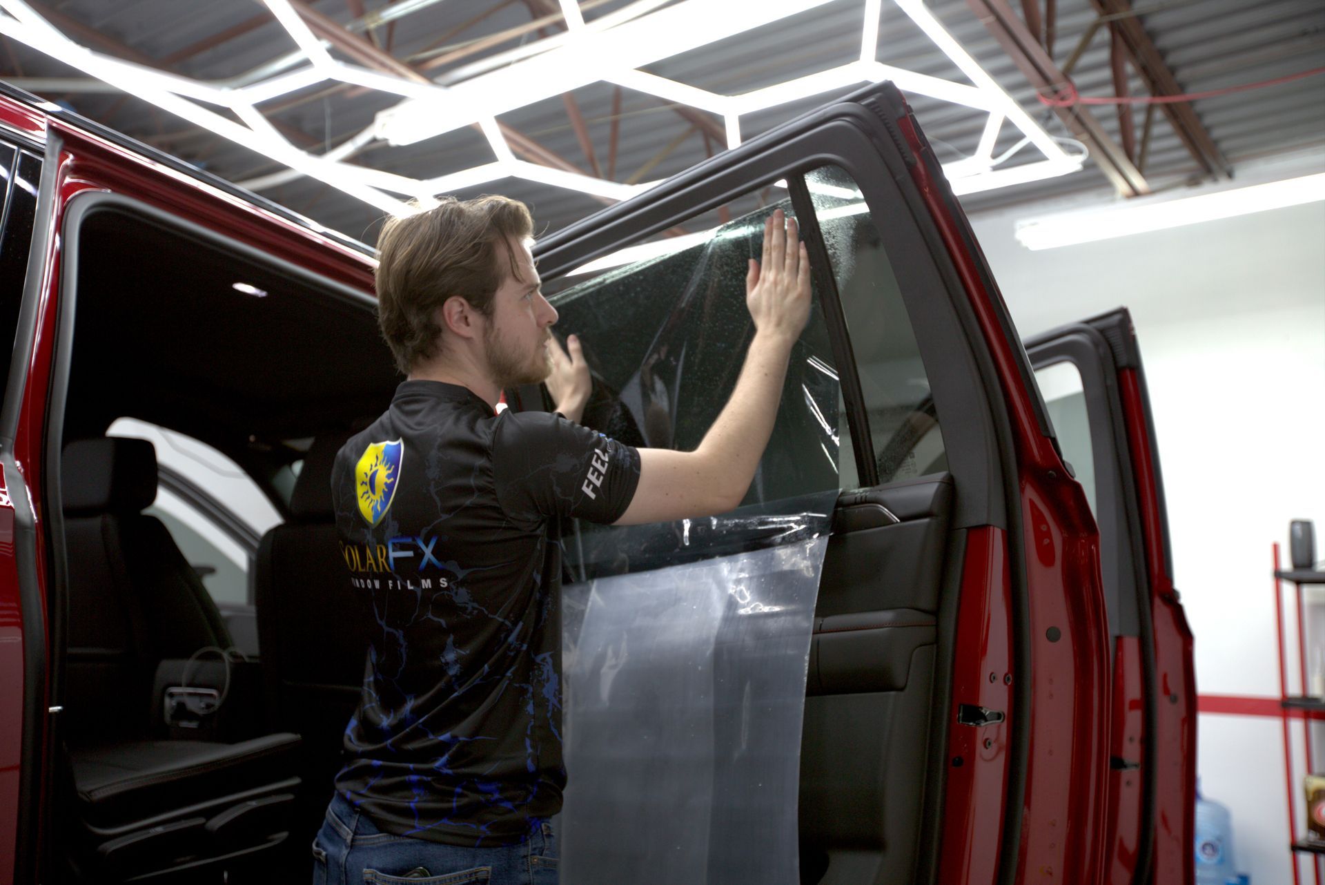 A man is applying window tinting to a red truck.