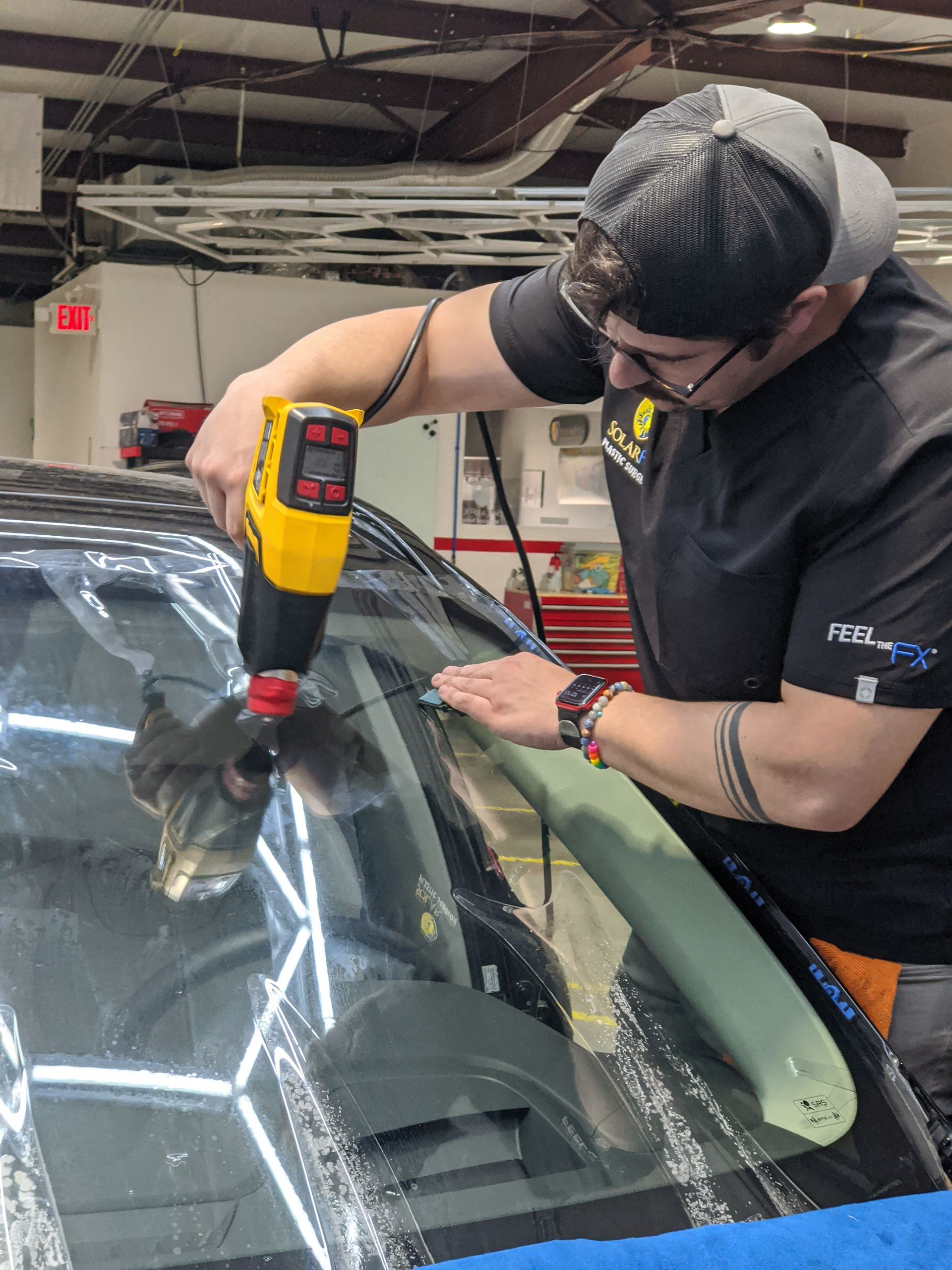 A man is using a drill to fix a windshield on a car.