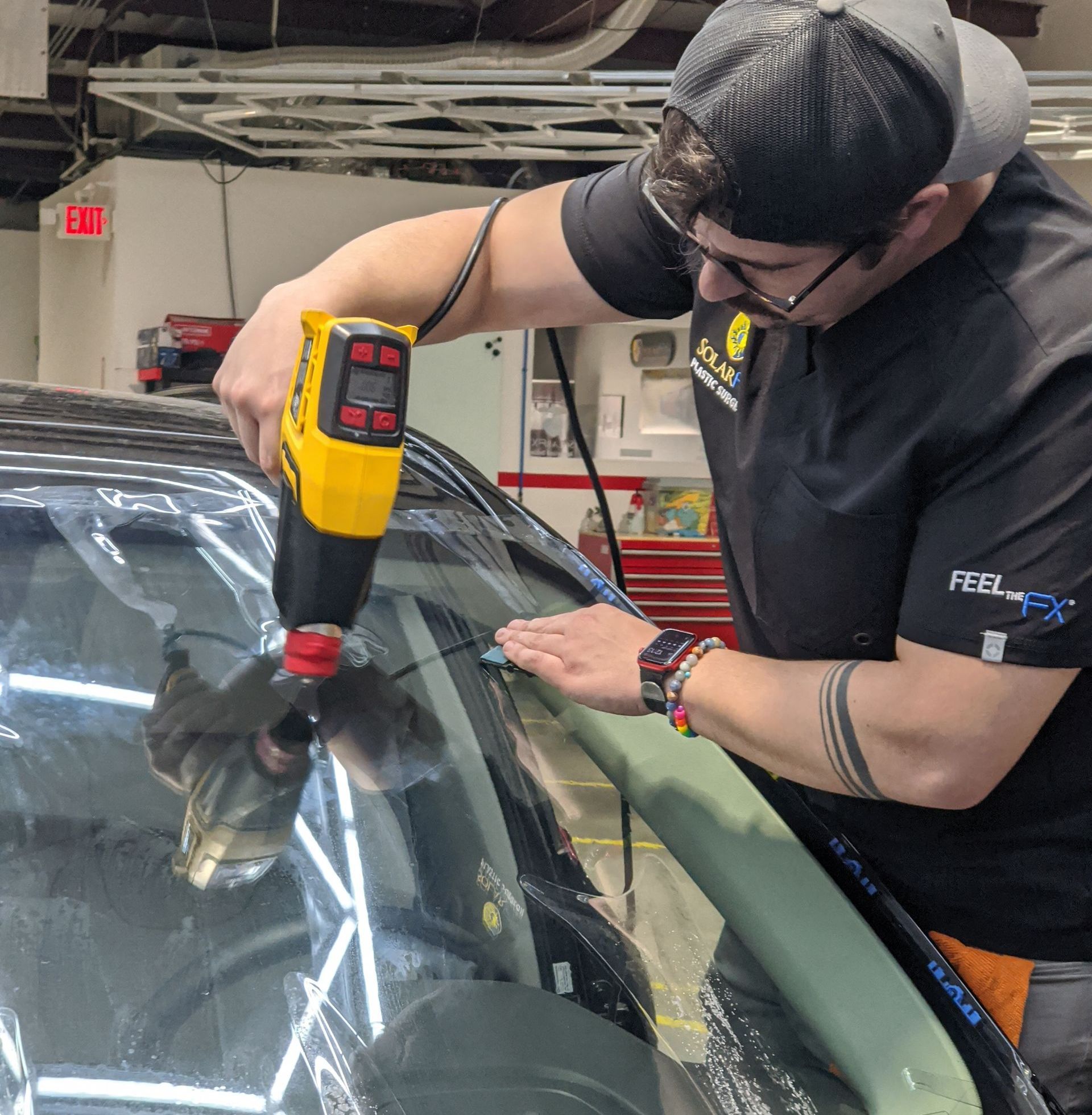 A man is using a drill to fix a windshield on a car.