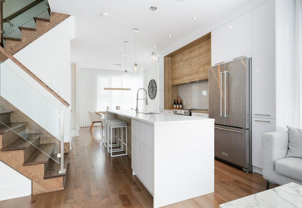 Une cuisine avec armoires blanches, électroménagers en acier inoxydable, un grand îlot et des escaliers.