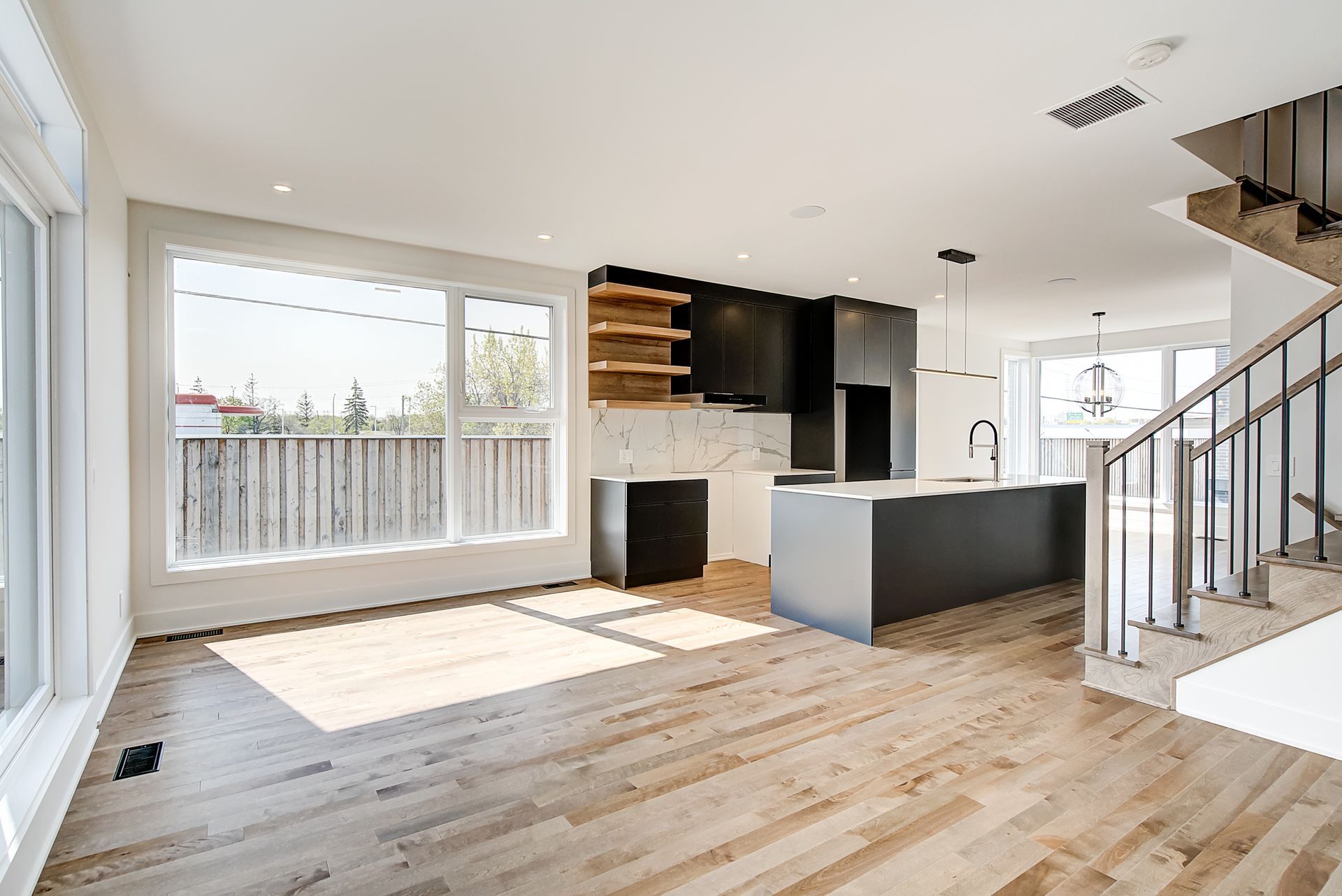 Un salon vide avec parquet et une cuisine en arrière-plan.