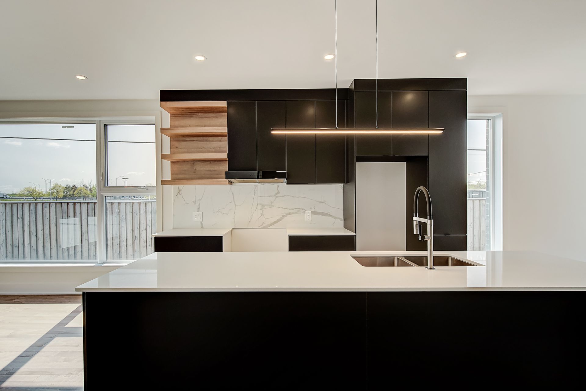 Une cuisine avec armoires noires, comptoirs blancs, un évier et un réfrigérateur.