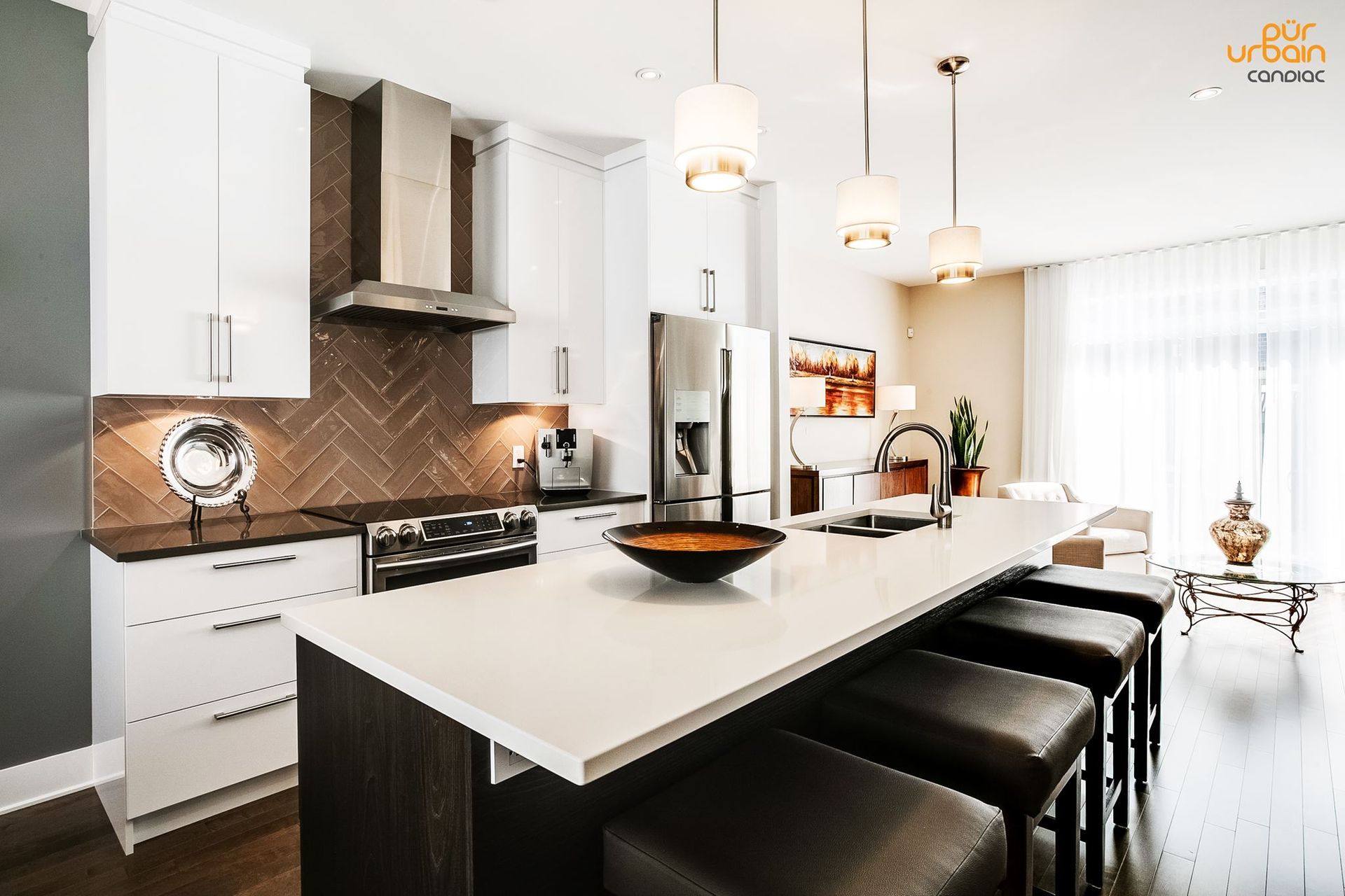 Une cuisine avec armoires blanches, comptoirs noirs, tabourets et un grand îlot.