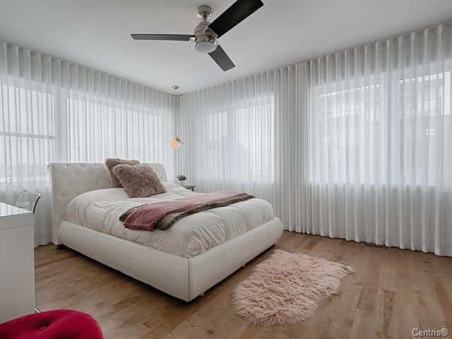 Une chambre avec un lit, un ventilateur de plafond et des rideaux blancs.