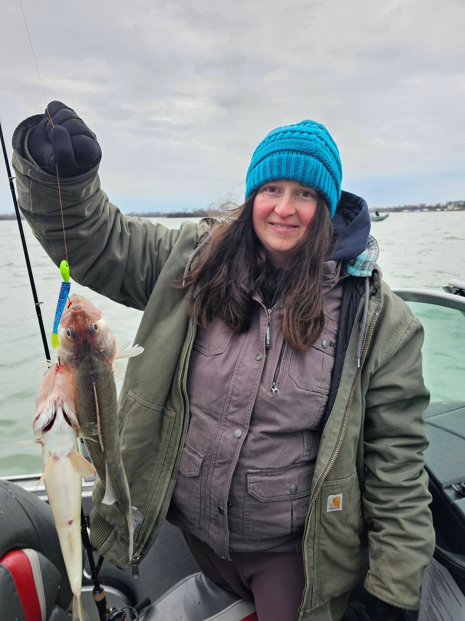 Person in a blue knit hat holding up a large fish while ice fishing on a snowy lake