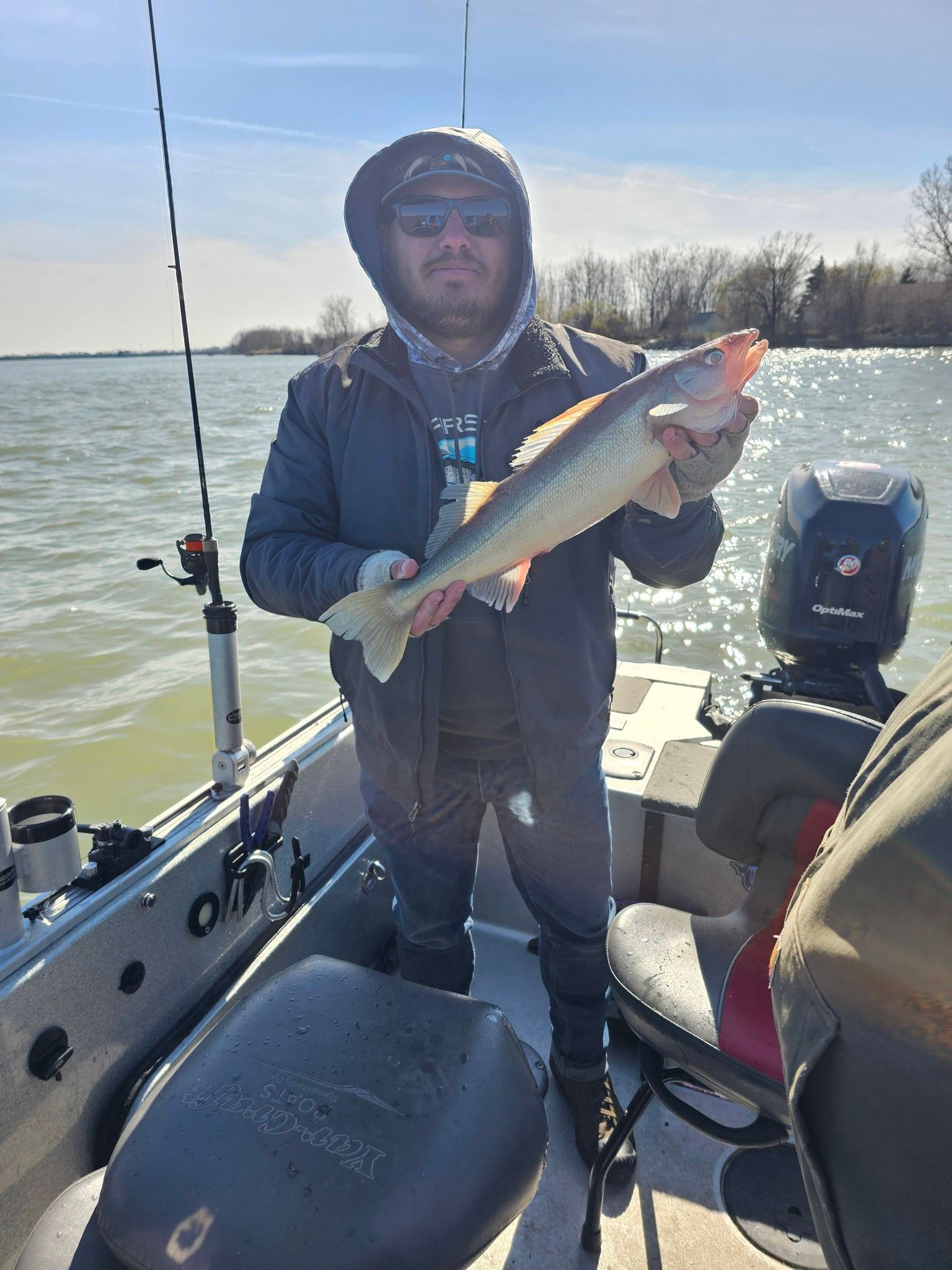 Person on a fishing boat holding a silver fish near open water on a sunny day