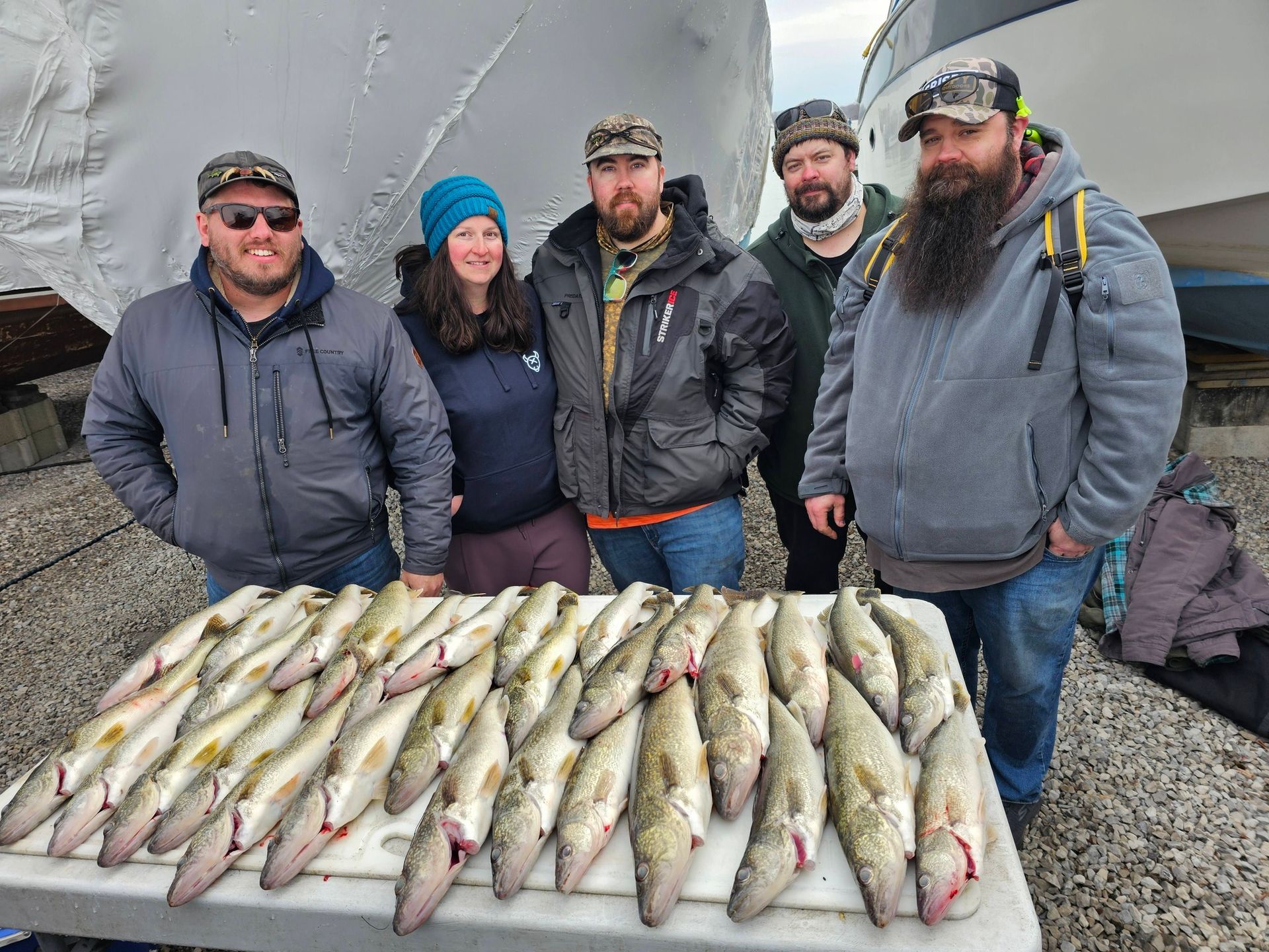 Five people posing behind a table covered with many fish outdoors on a rocky shore.