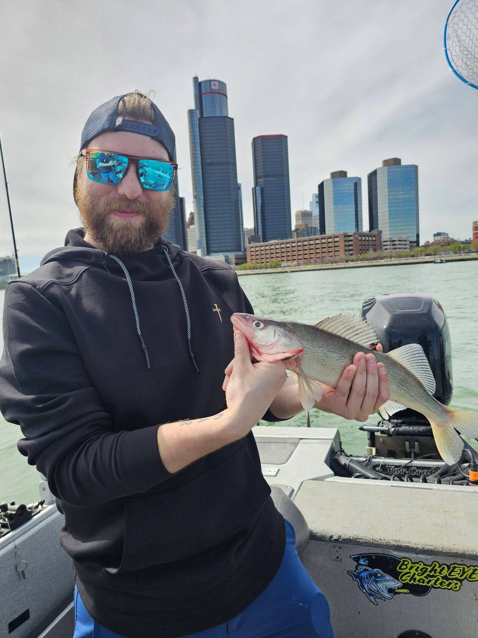 Person on a boat holding a fish, with a city skyline and water in the background.