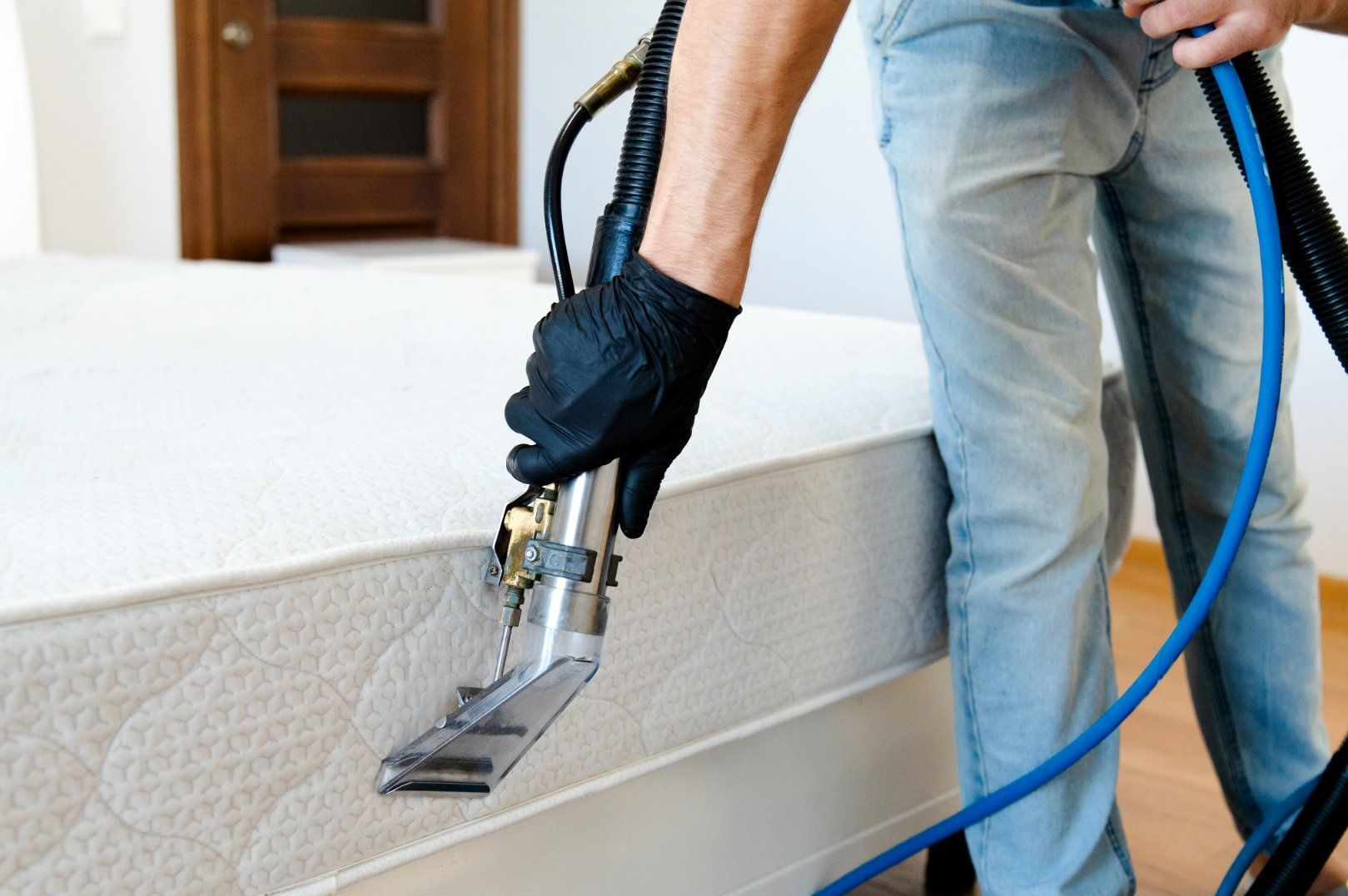 Person cleaning a white mattress with an industrial vacuum, close-up shot.
