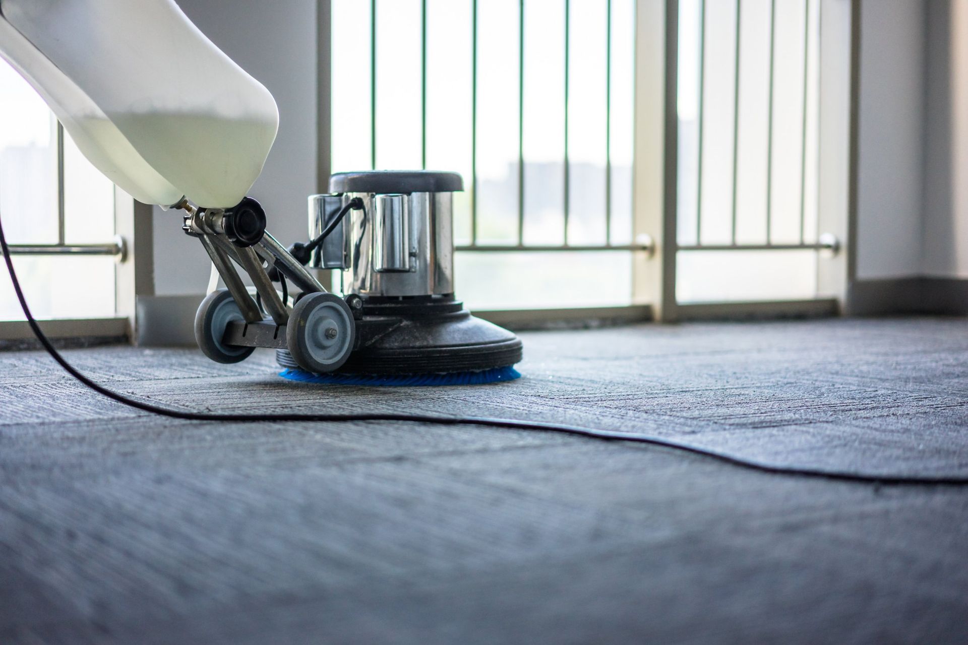 Floor cleaning machine, spraying cleaning solution onto a carpeted floor near a window.
