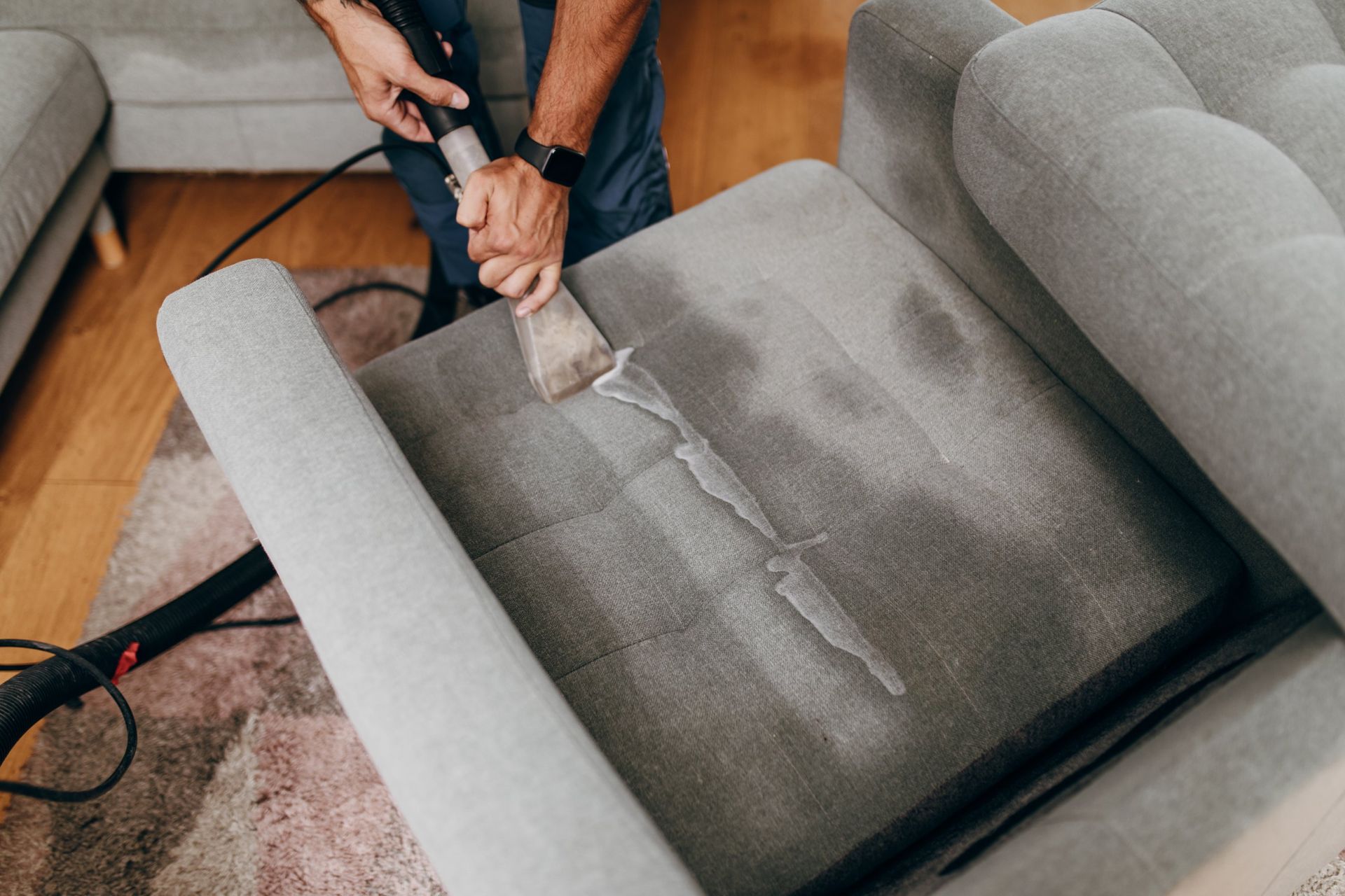 Person vacuuming a gray upholstered armchair in a home setting.