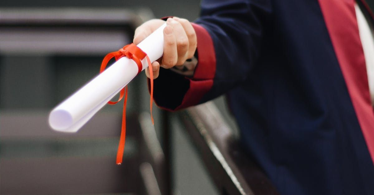 A person is holding a diploma with a red ribbon around it.