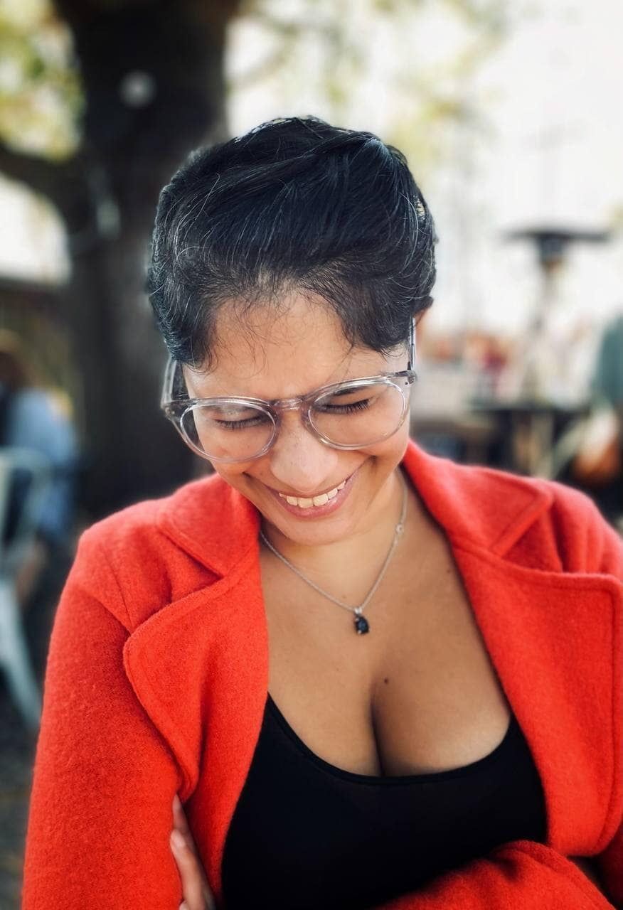 A woman wearing glasses and a red jacket is smiling