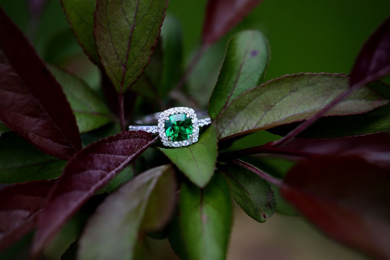 An emerald and diamond ring is sitting on a green leaf.