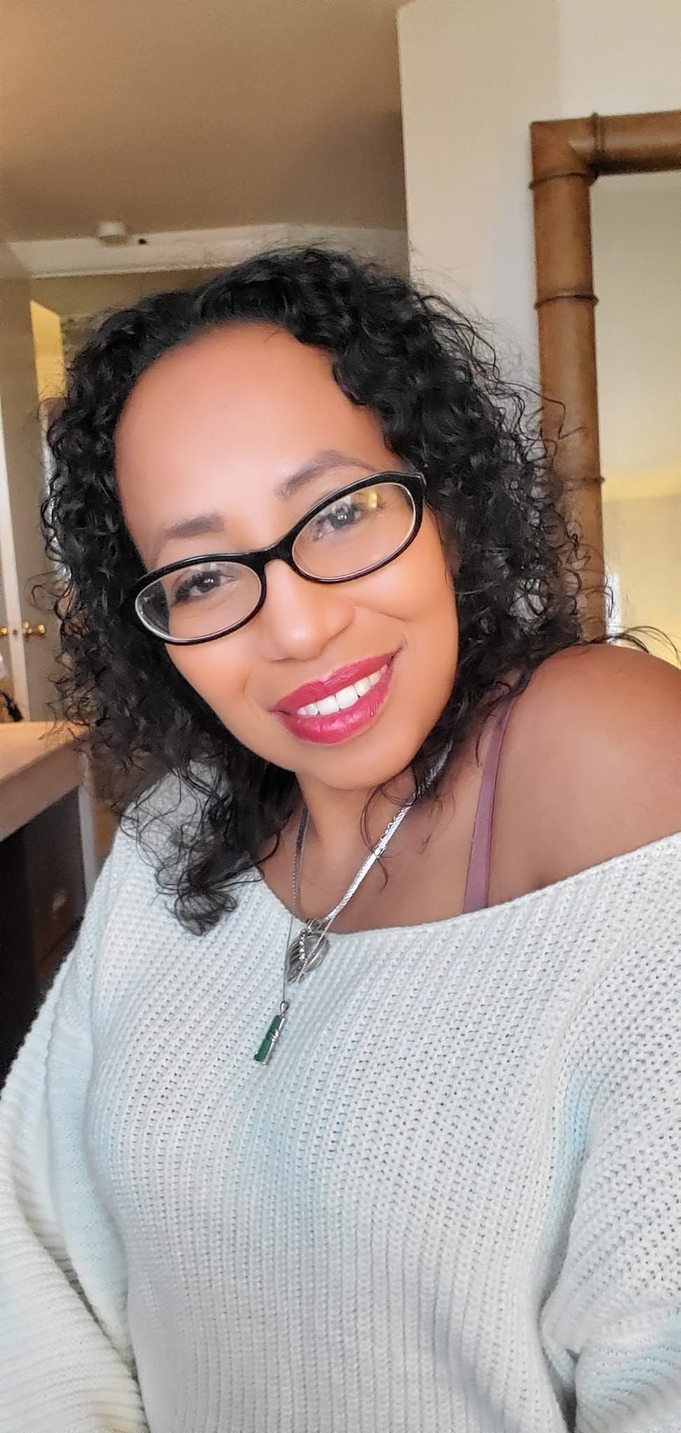 A woman wearing glasses and a white sweater is smiling for the camera.