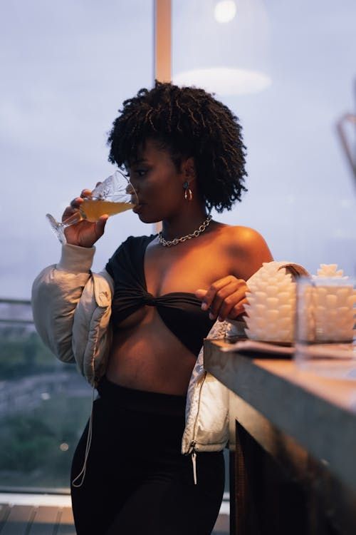 A woman in a crop top is drinking a glass of beer.