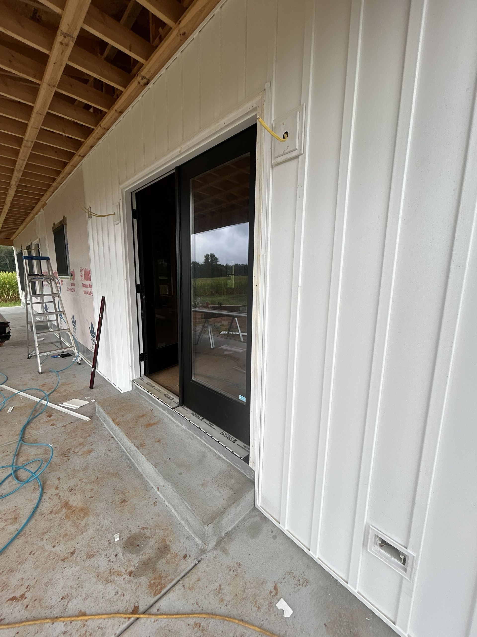 Partially finished building exterior with open sliding glass door and construction debris on the porch
