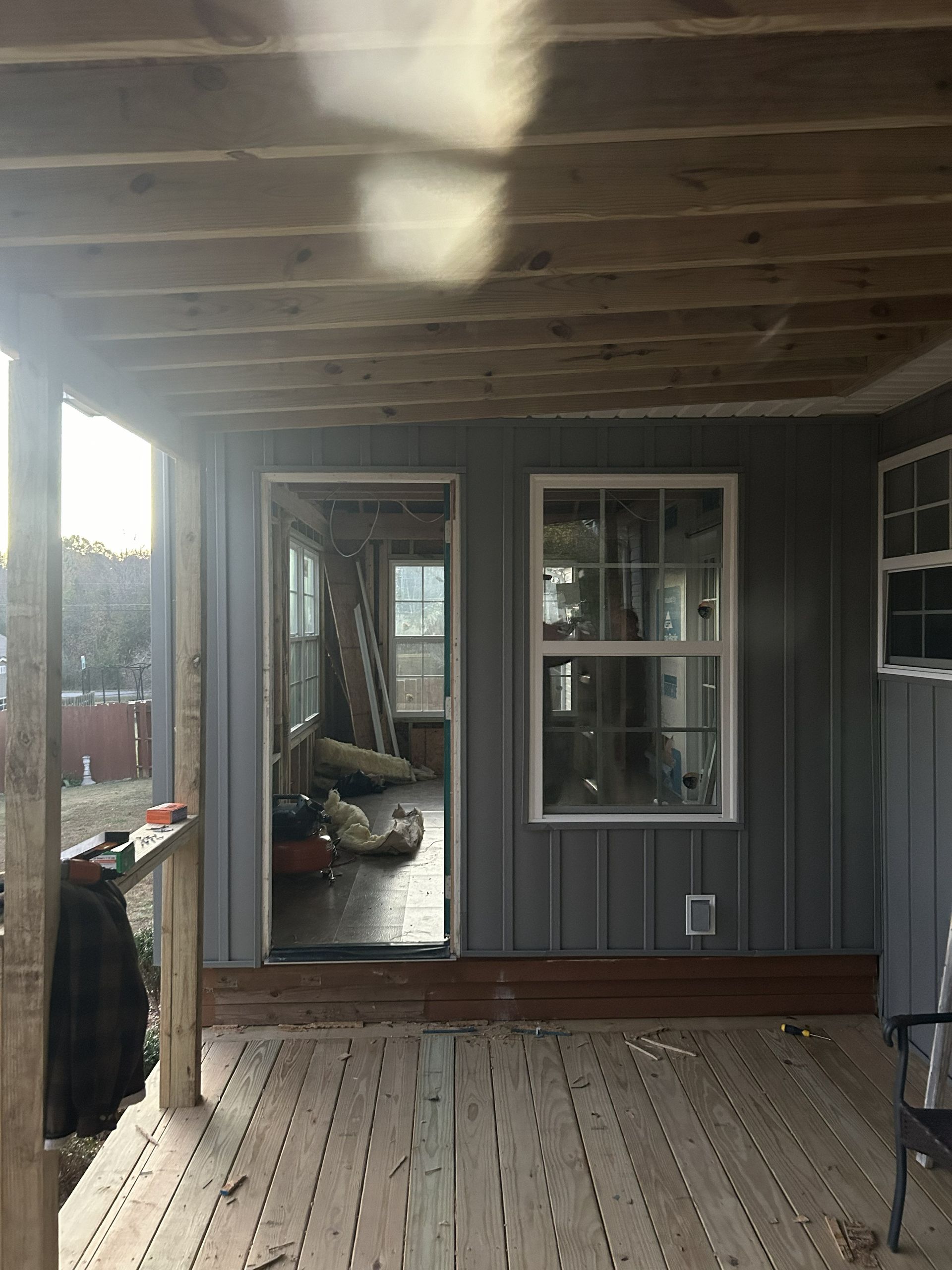 Covered wooden porch with gray siding, white-trimmed windows, and deck boards in warm sunlight